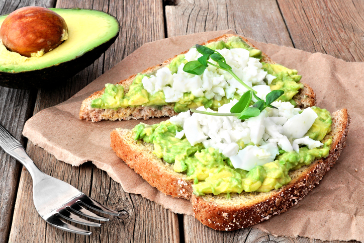 Avocado toast with egg whites and pea shoots on paper against a rustic wood background