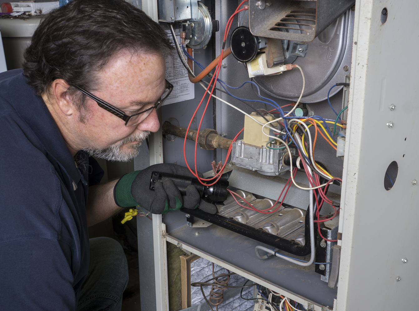 Techician looking over a gas furnace with a flashlight before cleaning it.